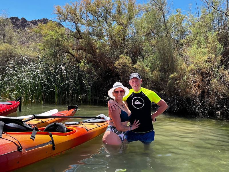 Black Canyon Kayak Tour - A smiling couple takes a refreshing break beside colorful kayaks in a peaceful riverside inlet.