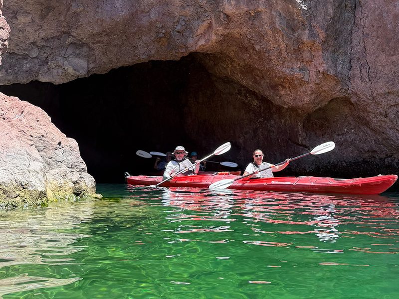 Black Canyon Kayak Tour - Kayakers emerge from a dramatic rock cave into clear green water beneath the desert sun.