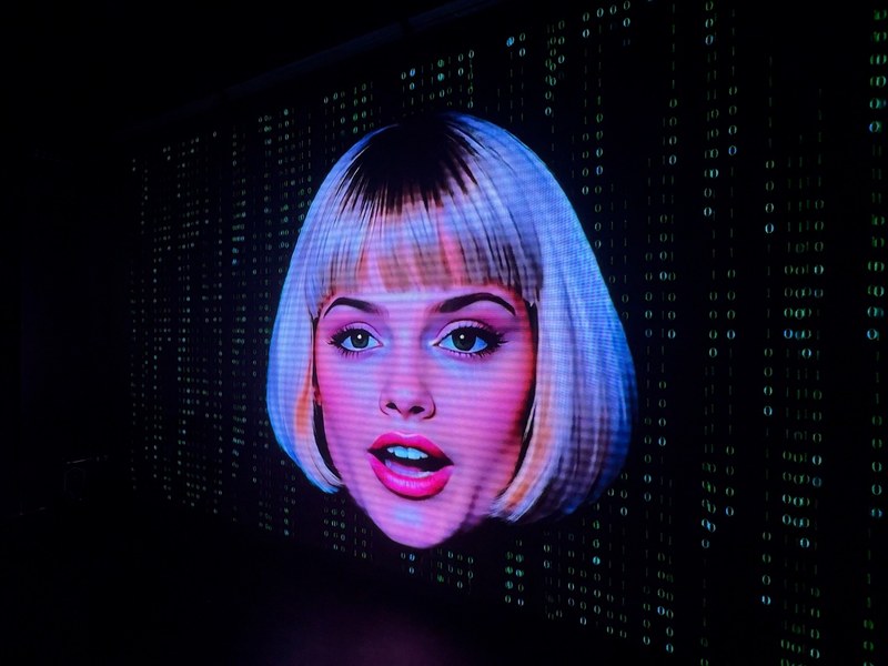 HACKED - LILA, HACKED’s AI magician, appears against a cascading digital code backdrop.