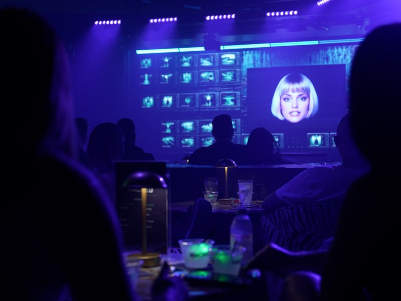 HACKED - Audience members watch LILA appear across HACKED’s futuristic stage screens.