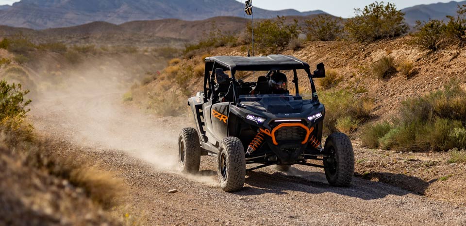 Off-road RZR buggy kicking up dust on a rugged Mojave Desert trail near Las Vegas