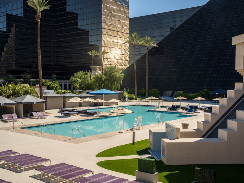 An elevated view showcases the expansive Oasis Pool complex framed by palms, lounge chairs, and Luxor's signature architecture.