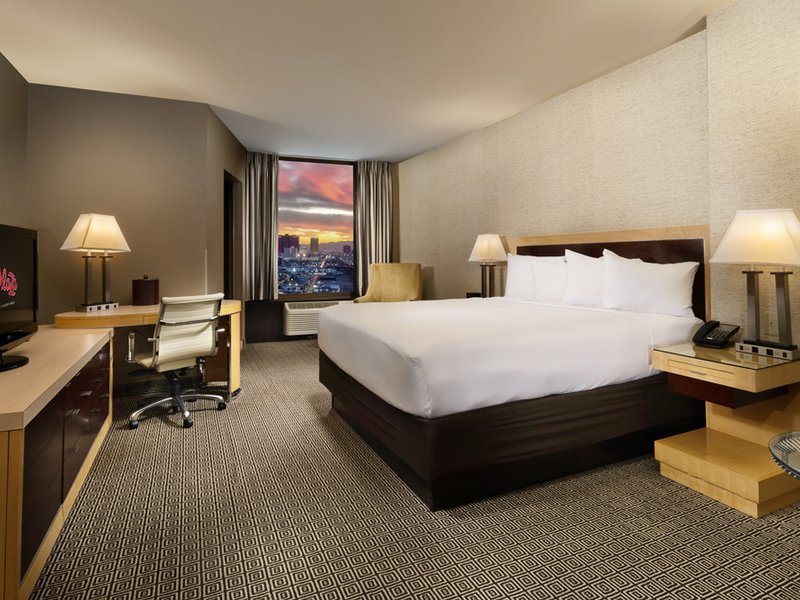 Spacious Deluxe King Room featuring modern furnishings, a dedicated workspace, and views of downtown Las Vegas.