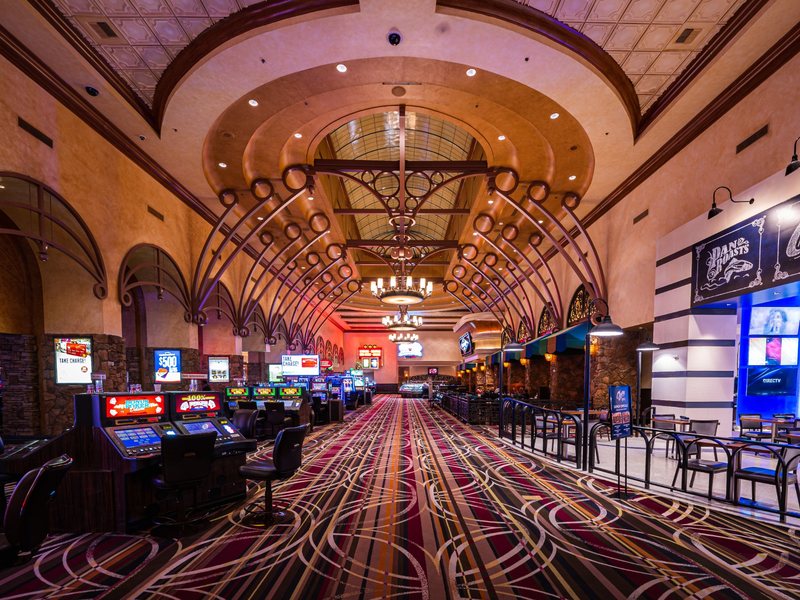 Rows of slot machines stretch beneath warm chandeliers and richly detailed ceilings on the Santa Fe Station casino floor.