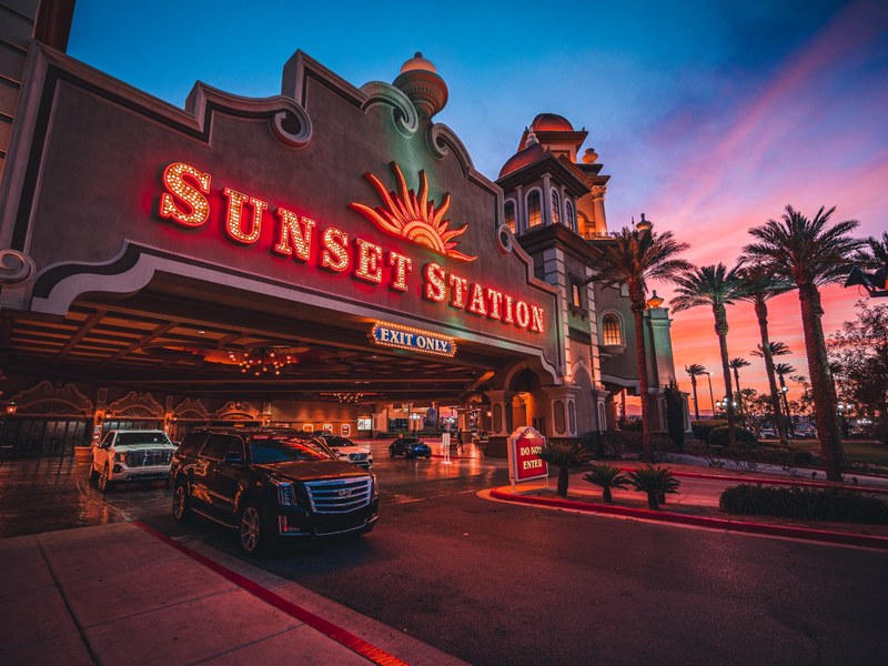 Sunset Station’s illuminated porte cochère welcomes guests beneath a colorful Las Vegas sunset, framed by palms and classic resort architecture.